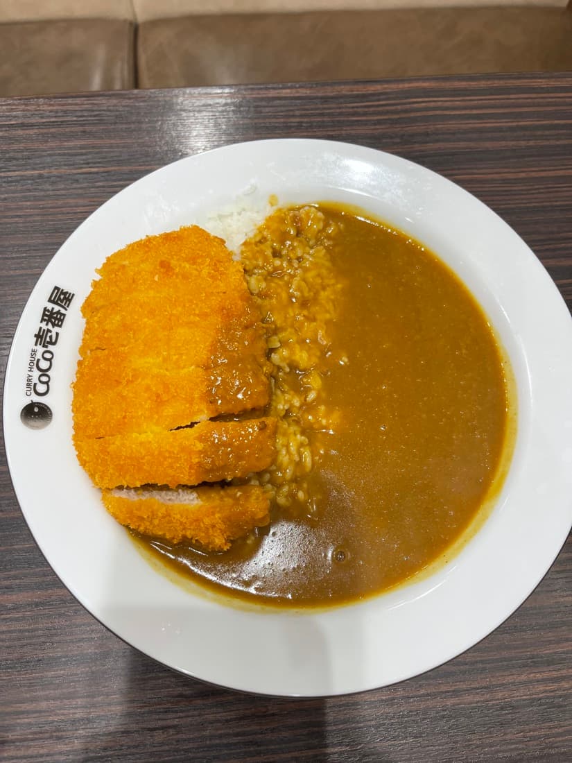 CoCo Ichibanya pork curry with rice and a sliced breaded pork cutlet on a white plate